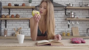 Kitap okuma ve mutfakta yeşil elma yiyen kadın iç çamaşırı sevimli genç kadın portre. Genç Bayan, sağlıklı bir yaşam tarzı. Eğlence genç güzel yalnız kızın.
