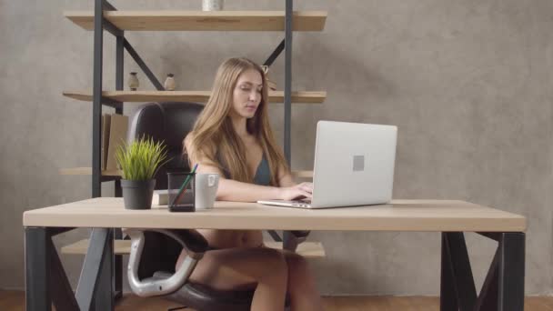 Ładna dziewczyna w bieliźnie, siedząc w czarne skórzane krzesło przy stole, działa na jej laptopie w nowoczesnych pokojach w domu. Wypoczynek z ładna pani. Młody sekretarz pracy na luzie w stylu wolnym. — Wideo stockowe