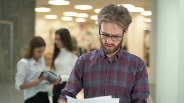 Nespokojený manažer recenzování dokumentů v hale obchodního centra. Portrét vousatého zmateně obchodníka s brýlemi s nelibostí při pohledu na papír. — Stock video