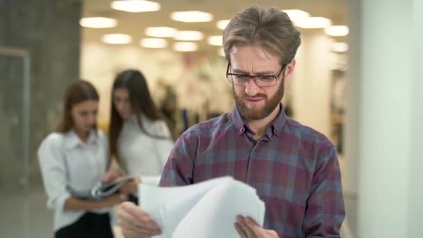 El gerente barbudo jura y rechaza el contrato. Retrato de un administrador molesto de pie en el vestíbulo de un centro de negocios en el fondo de dos niñas que se comunican entre sí — Vídeo de stock