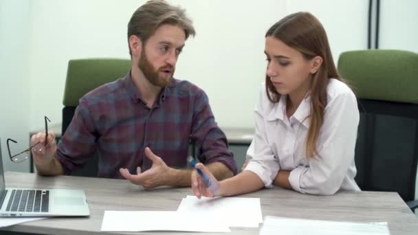 El jefe barbudo apunta a la pantalla de un portátil mientras se enfoca en su personal en aspectos de la nueva estrategia. Subordinate colega está registrando en papel los principales aspectos de la propuesta de negocio . — Vídeos de Stock