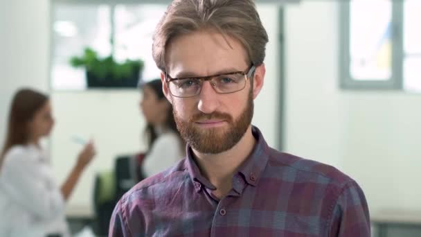 Portrét mladé atraktivní seriózní člověk, dotýká jeho vlasy v úřadu na pozadí dvou jeho kolegové — Stock video