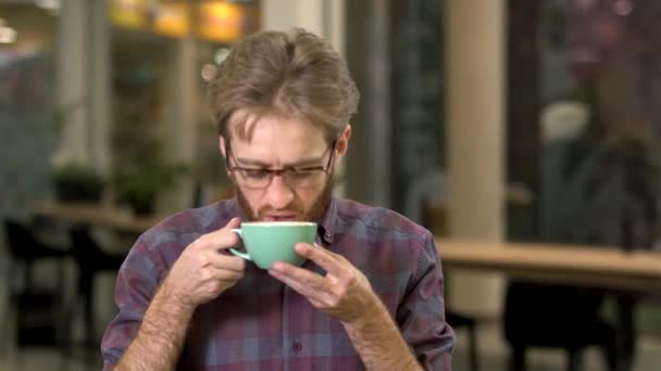 Retrato de un joven atractivo bebiendo sabroso capuchino caliente después de un duro día de trabajo y sonriendo con placer — Vídeos de Stock