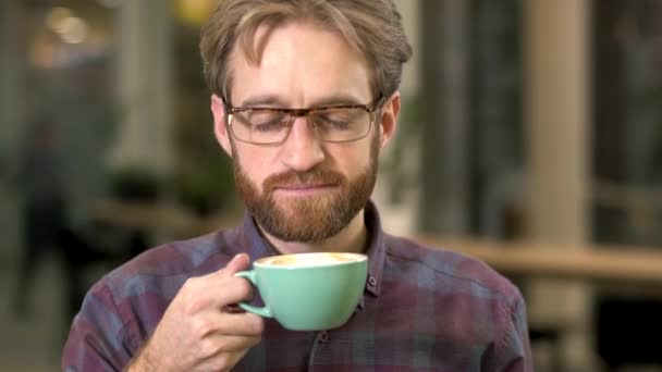Ritratto di un ragazzo barbuto sorridente in bicchieri che beve caffè con piacere . — Video Stock