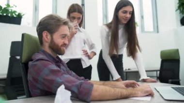 Sakallı bir adam ve iki genç kız işyerinde ofiste iş planı görüşüyorlar.