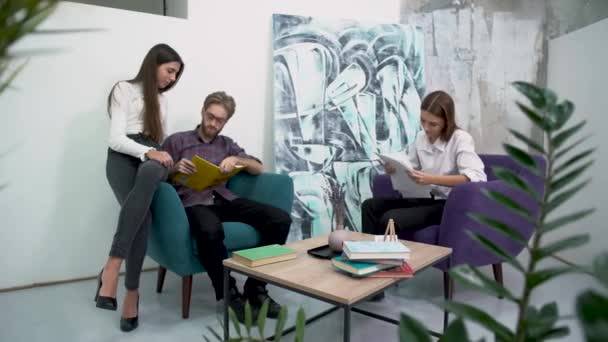 Office workers have a break sitting in comfortable armchairs and talk with each other. Discussion of work plans in a relaxed atmosphere. — Stock Video