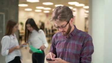 Ciddi genç adam gözlüklü ve rahat ekose gömlek tribünlerde bir hub sakallı ve manifatura mesaj üzerinde duruldu. Arka plan üzerinde iki kadın arkadaşları birbirleri ile konuşuyorsun.