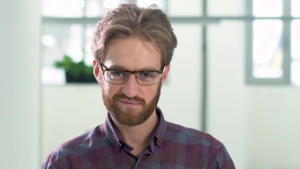 Portrait a smilling bearded guy with glasses in a daily plaid shirt standing in the office center in the lobby on a white background. — Stock Video