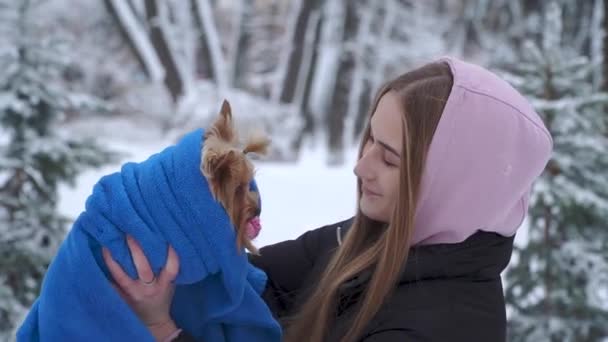 Portret meisje kussen een yorkshire Terriër in een winter met sneeuw bedekte park houden van een hond die zijn verpakt in een blauwe deken. Een tiener en een huisdier op een wandeling buiten. Slow motion. — Stockvideo