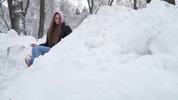 Νεαρή γυναίκα που καπνίζει στον πάγκο σε ένα χειμώνα χιονισμένο πάρκο. Γιορκσαιρ Τεριε περπατά κοντά στα πόδια του ιδιοκτήτη. Έφηβος και ένα σκυλί που αναπαύεται σε εξωτερικούς χώρους μαζί. Αργή κίνηση. — Αρχείο Βίντεο