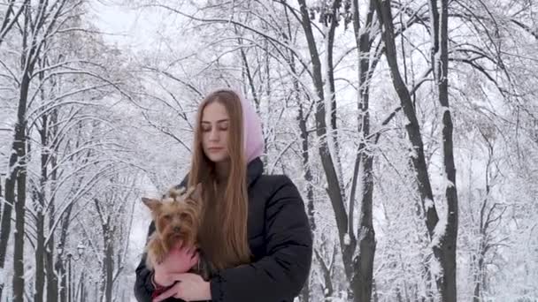 Teen dziewczyna portret przytrzymanie yorkshire terrier ręce na tle ośnieżonych drzew w parku zimowym. Nastolatek i zwierzętom na spacer na świeżym powietrzu. Zwolnionym tempie. — Wideo stockowe