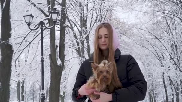 세로 귀여운 십 대 소녀 요크 셔 테리어를 들고 겨울 공원에서 눈 덮힌 나무의 배경에 손. 십 대 그리고 야외 산책에 애완 동물. 슬로우 모션. — 비디오