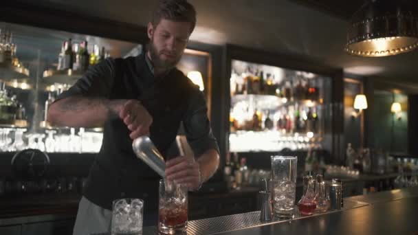 Hezký barman přidáním velké kostky ledu dělat koktejl v krásném moderním baru whisky. Zpomalený pohyb — Stock video