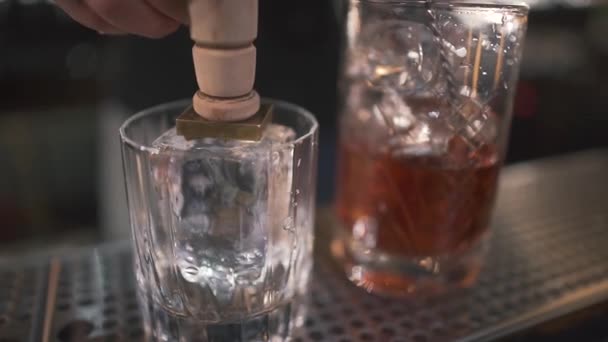 Unrecognizable bartender pricking ice for coctails with icebreaker in glass for alcohol shots in modern bar. Close up — Stock Video