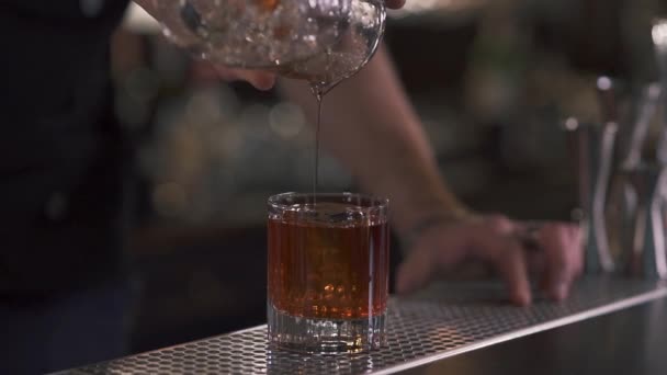 Manlig hand bartendern häller vätska i glaset med stor isbit i det närbild. Bartendern att göra alkoholhaltiga cocktail i moderna bar. Närbild. — Stockvideo