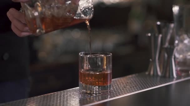 Cantinero vertiendo un refrescante whisky o cóctel de alcohol en un vaso con hielo. De cerca. Movimiento lento — Vídeos de Stock