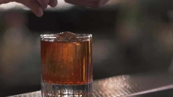 Male hand puts orange slice into a glass with a cocktail or whiskey close up. — Stock Video
