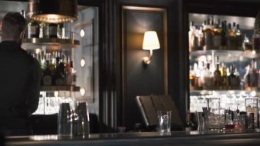 Uzun boylu barmen gerekli şişe alkol seçme yuvarlak raf alır. Barmen raflarda birçok şişe ile modern barda kokteyl yapmak