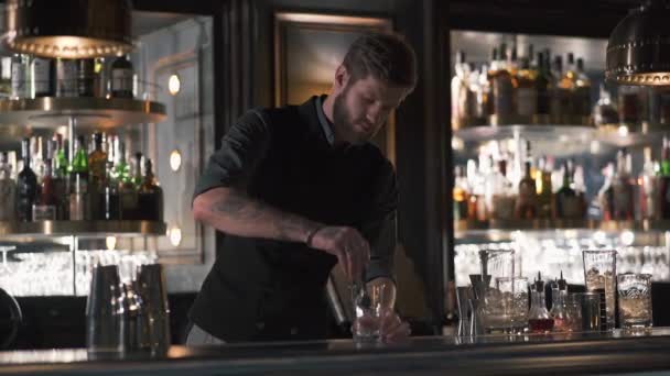 Mélangeur barman attrayant ajoutant un gros cube de glace pour préparer un cocktail dans un beau bar moderne. Mouvement lent — Video