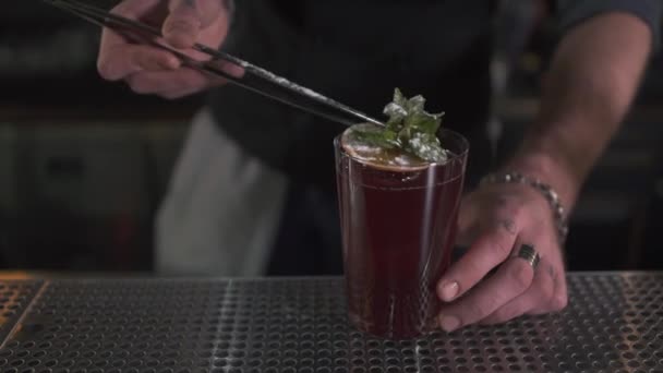 Mannenhand versieren verse cocktail met mint en oranje Tang met toog close-up. Barman maken cocktail in de moderne bar staande in de buurt van teller. Man voorbereiding alcohol drinken voor client — Stockvideo