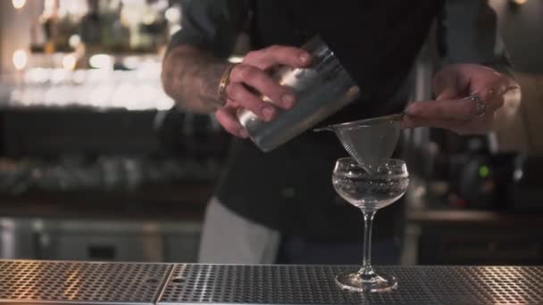 Barman versant un cocktail de lait rose à travers un tamis en verre haut sur comptoir de bar fermer. Les mouvements des hommes sont très précis, le verre est rempli exactement au sommet — Video