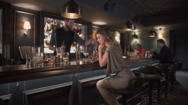 Malzemeyi birleştirerek ve kokteyller yapma hipster barmen genç kadın oldukça süre bar sayacı ve exting ileti çubuğu yakınındaki oturur