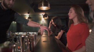 Üç güzel iyi giyimli genç kız barın oturmak ve güzel hipster barmen onları tek tek bir kokteyl verdi