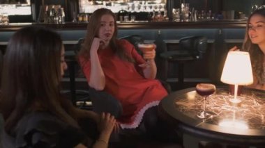 Üç güzel iyi giyimli genç kız barın yakınında rahat masa, içki kokteyl ve hayat hakkında sohbet tarafından oturmak