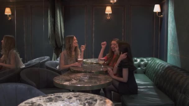 Tres mujeres alegres sentadas en la pequeña mesa de la cafetería y conversando. Las niñas tienen celebración, charlan y sonríen sentadas en un lugar privado en un cómodo sofá. Las damas solitarias se divierten. — Vídeos de Stock