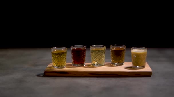 Gros plan cinq différents coups alcooliques coctails dans de petits verres debout sur le bureau isolé sur fond noir . — Video