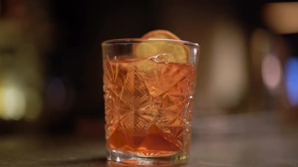 Alkoholschuss mit Orange und Eis aus nächster Nähe auf dem Tisch. Barkeeper steckt Zimt ins Glas — Stockvideo