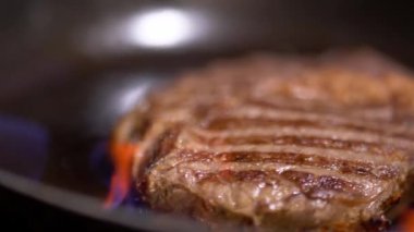 Sulu bir kalbur yalan et parçası olan bir ateşi canlandıran kızarmış. Kamera soldan sağa taşır. Yakın çekim.