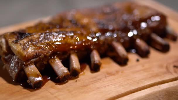 Close-up gewoon gekookt sappige geurige gebakken ribben gedrenkt met barbecue saus. Prachtig serveren op houten bureau. — Stockvideo