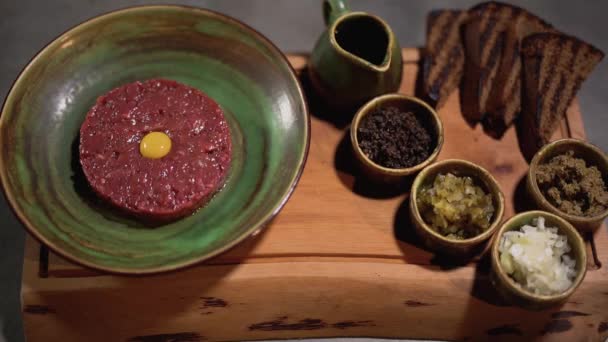 Le jaune d'oeuf tombe dans le tartare cru et les ingrédients se trouvent dans des tablettes d'argile sur la table de cuisine. Ferme là. Concept culinaire et culinaire . — Video