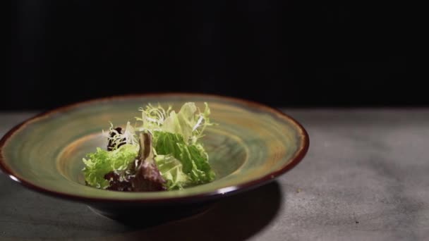 Foglie di cavolo e lattuga in un piatto di argilla in piedi sul tavolo della cucina isolato su uno sfondo nero. Da vicino. . — Video Stock