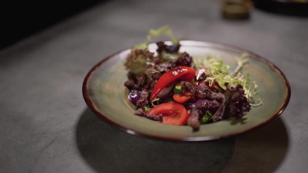 Салатні інгредієнти потрапляють в тарілку, що стоїть на поверхні столу. Приготування їжі крупним планом — стокове відео