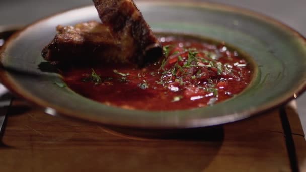 Unrecognized cook puts the pork rib in the plate with delicious red borsch. Close up. — Stock Video