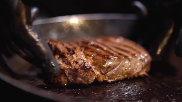 Τα χέρια σε μαύρο τροφίμων γάντια παραμόρφωσης ένα κομμάτι κρέας στο τηγάνι, κοντινό πλάνο — Αρχείο Βίντεο
