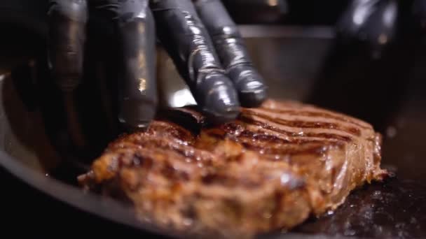Hand in black food gloves press a piece of meat lying on the pan close up — Stock Video