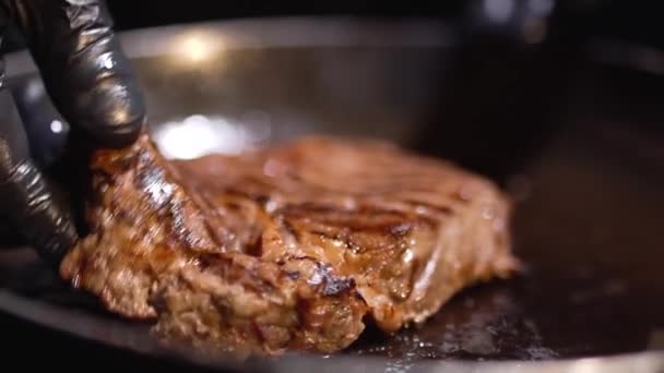 Рука в черных пищевых перчатках превращает кусок мяса, лежащий на сковороде с другой стороны близко — стоковое видео