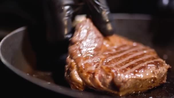 Close-up van de hand in zwarte rubberen handschoenen houden heerlijke gebakken biefstuk over koekenpan. — Stockvideo