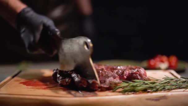 Manlig hand i svart gummihandskar separerar köttbitarna ligga på skärbrädan med en skärande kniv. Närbild. Slow motion. — Stockvideo