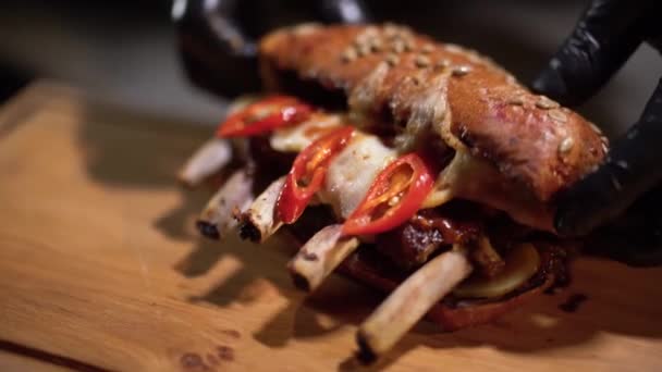 Händer i svart gummihandskar lyfta toppen av en stor smörgås med grillad nötkött revben Slow motion. Närbild. — Stockvideo