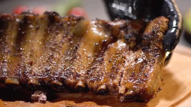 Tűzhely kezét kesztyű fekete élelmiszer bizonyítja, tökéletes finom grillezett bordát közelről — Stock videók