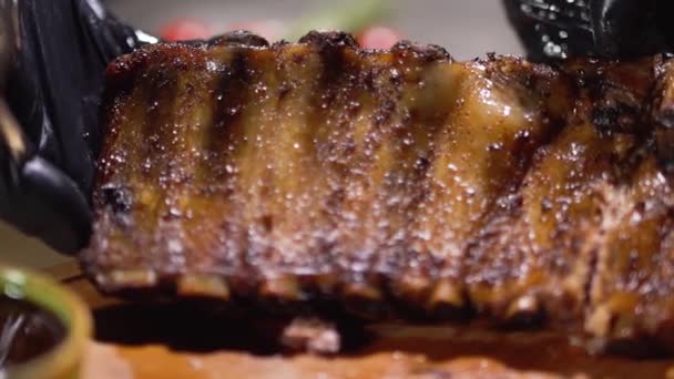 Руки повара в черных перчатках для еды демонстрируют превосходные сочные вкусные жареные ребрышки вблизи — стоковое видео