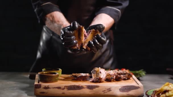 Las manos masculinas en guantes de goma negro desgarran sabrosas costillas asadas de cerca. Movimiento lento . — Vídeos de Stock