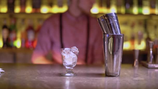 Glas met ijs en metaal shakers zijn op de bar teller. Barman reinigt het glas op de achtergrond — Stockvideo