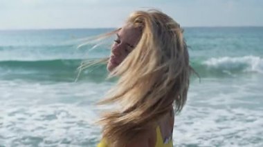 Genç sarışın kadın başını, deniz arka planda çırpınan saç yapma sallıyor. Yalnız kız denizde vakit geçiriyor. Eğlence genç kız