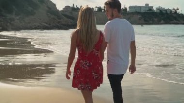 Genç çift elele günbatımı doğru birbirleriyle konuşan ve having fun boş kum plajı üzerinde yürüme. Ağır çekim