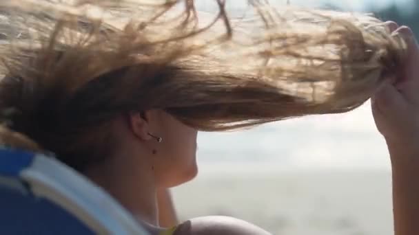 Muchacha joven atractiva endereza su cabello en el viento y disfruta del maravilloso clima junto al mar. En cámara lenta. De cerca. — Vídeo de stock
